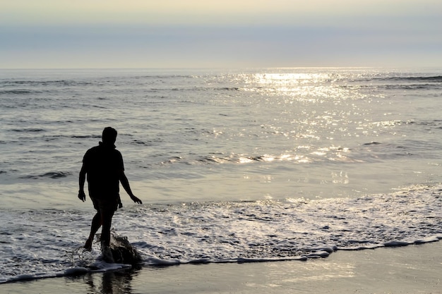 sagoma di un uomo che cammina lungo la riva del mare al tramonto