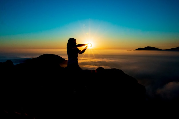 sagoma di una donna che prende il sole con le mani in cima a una montagna