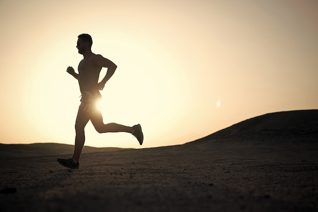 Sagoma di uomo che corre sullo sfondo del cielo infuocato al tramonto in montagna, sport e ricreazione, futuro e successo, persone e natura, velocità e stile di vita sano