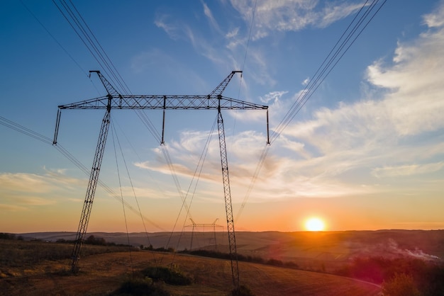 Sagoma scura della torre ad alta tensione con linee elettriche all'alba Trasmissione del concetto di energia elettrica