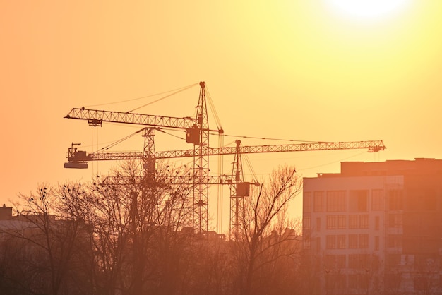 Sagoma scura di gru a torre in alto cantiere di edifici residenziali al tramonto Sviluppo immobiliare