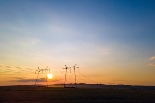 Sagoma scura di torri ad alta tensione con linee elettriche all'alba.