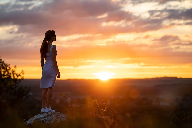 Sagoma scura di una giovane donna in abito estivo in piedi all'aperto godendosi la vista della natura