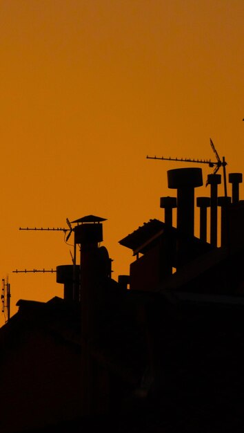 Sagome di antenne camini e tetti sotto un cielo al tramonto Duo tone