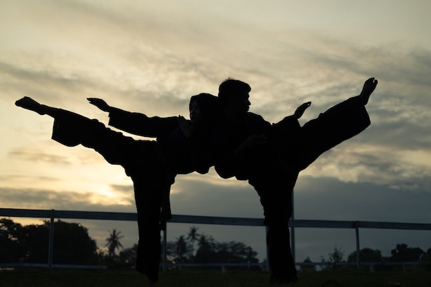 Sagome di due combattenti con movimento di calcio alto al tramonto