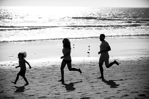 Sagome di famiglia che fanno jogging lungo la spiaggia del mare all'alba Sagome di allenamento all'aperto di corridori spor