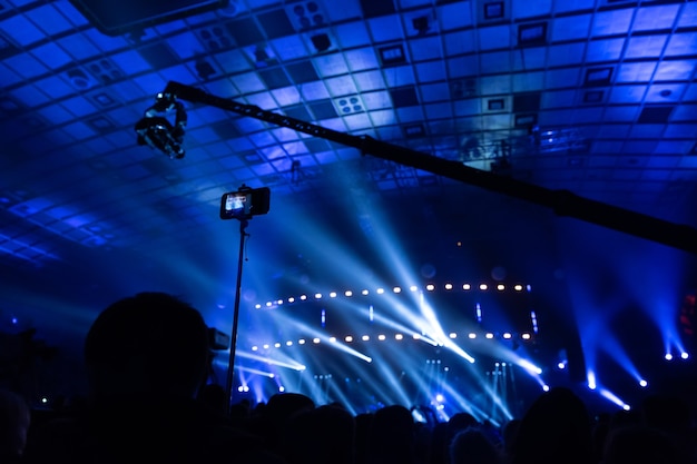 Sagome di folle di spettatori a un concerto con gli smartphone in mano. La scena è splendidamente illuminata da faretti.