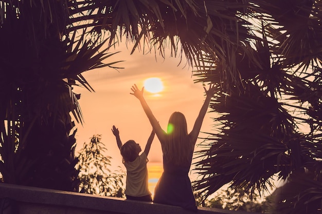 Sagome di madre e figlio, che incontrano il tramonto ai tropici sullo sfondo delle palme