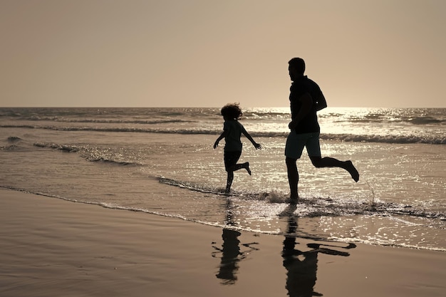 Sagome di padre e figlio che corrono divertendosi e sentono la libertà durante le vacanze estive sulla spiaggia estiva