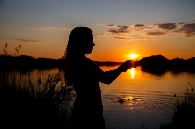 Sagome di ragazze al tramonto sul lago, il sole tramonta dietro gli alberi e splendidi riflessi nell'acqua