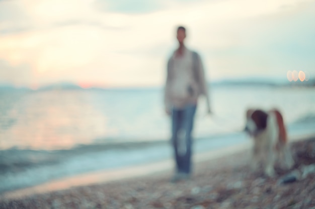 Sagome di uomo e cane che camminano lungo la riva del mare. Passeggiata serale al tramonto.