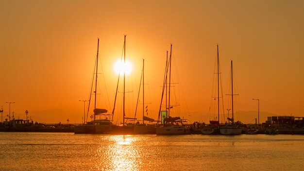 Sagome di yacht con alberi alti al tramonto nel porto