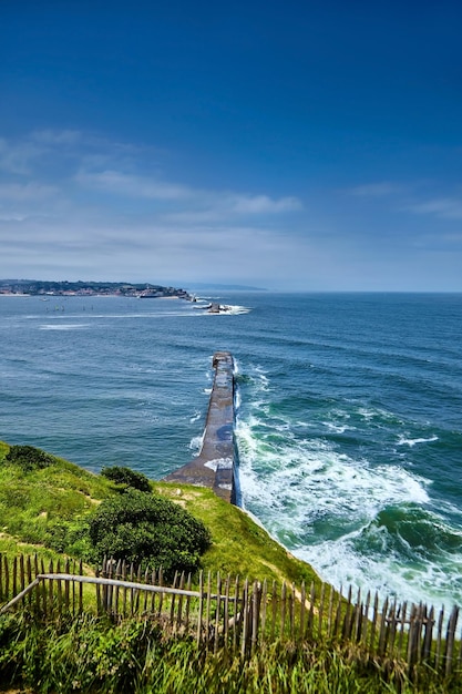 Saint Jean de Luz Francia Paese basco Erba verde sulla collina e onde dell'oceano che rompono la diga