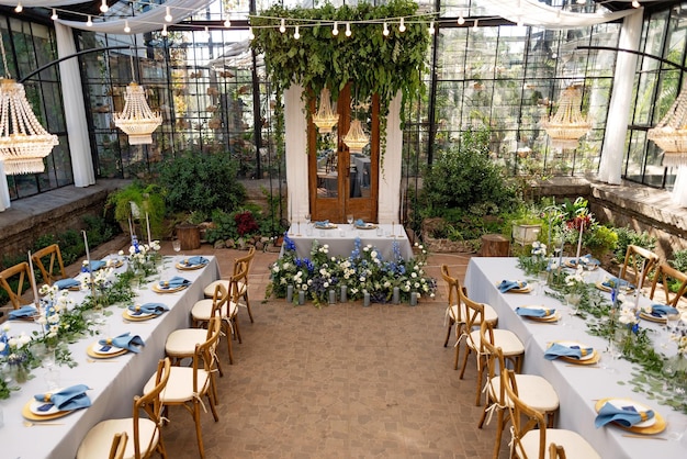 Sala per banchetti nuziali nella serra, i tavoli sono apparecchiati, decorati con fiori freschi, candele, lampadari di cristallo. Messa a fuoco selettiva morbida.