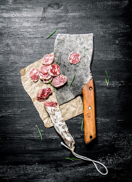 Salame con aglio e una vecchia accetta sulla tavola rustica nera.