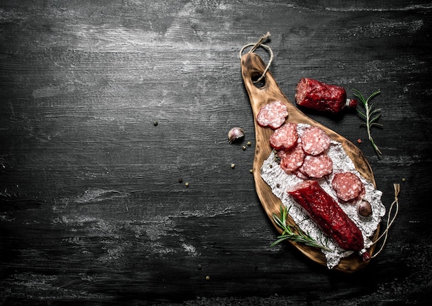 Salame con rosmarino fresco e spezie sulla tavola rustica nera.