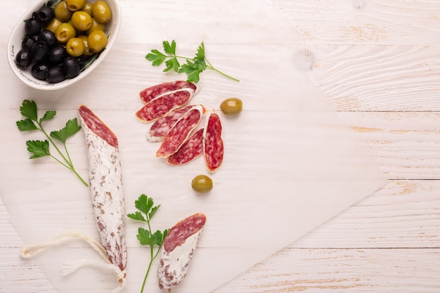 Salame e pane su fondo di legno bianco. Vista dall&#39;alto.