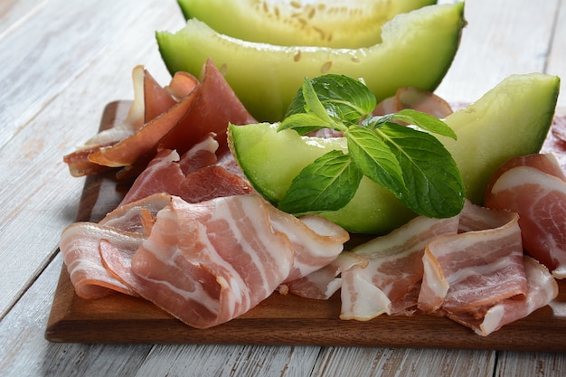 Salame, prosciutto, pancetta servita con melone e menta sul tagliere. Pranzo italiano