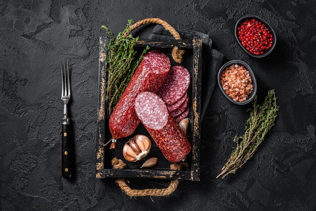 Salame secco a fette con timo fresco. Sfondo nero. Vista dall'alto.