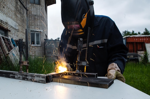 Saldatore di metalli che lavora con una saldatrice ad arco per saldare l'acciaio in fabbrica indossando dispositivi di sicurezza.