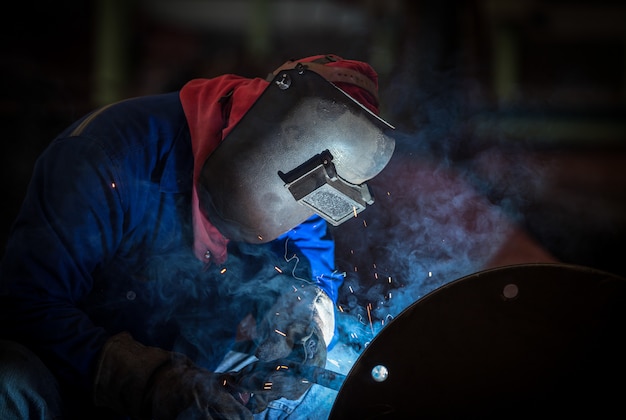 Saldatore industriale in fabbrica, giunto in acciaio saldato con maschera protettiva di sicurezza
