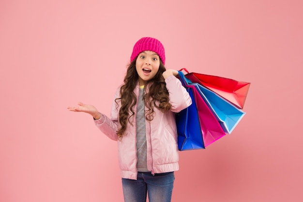 Saldi e sconti. Bambino felice. Bambina con regali. Acquisti invernali. Concetto di consumatore dell'acquirente. Saldi di Natale. Moda per bambini. Risparmio sull'acquisto delle vacanze. Acquisto a casa. Piccola ragazza con borse della spesa.