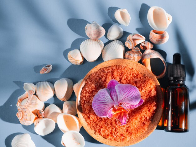 Sale da bagno arancione in un piattino con conchiglie e fiori su sfondo blu con un'ombra da una pianta tropicale. Copyspace, flatlay. Spa, rilassata, estate