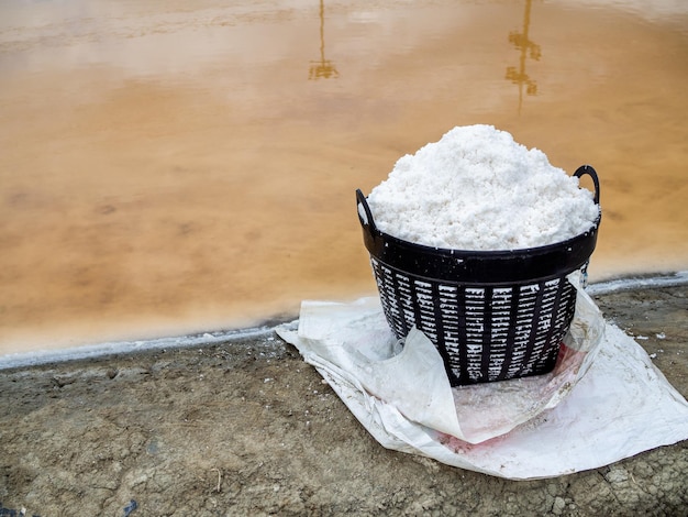 Sale marino bianco in cesto di plastica vicino a stagni di evaporazione del sale Concetto di produzione del processo di sale per l'agricoltura del sale