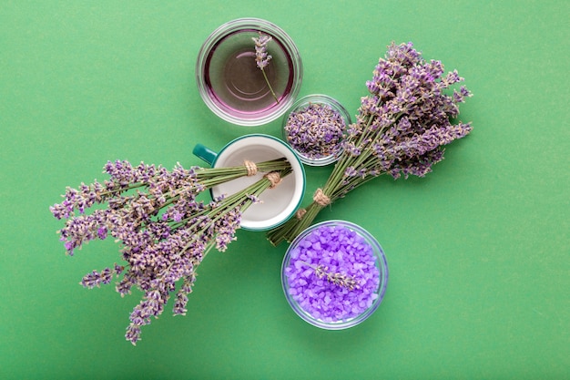 Sale marino viola lavanda con fiori di lavanda freschi e secchi, liquido di olio essenziale su sfondo di colore verde. Trattamento aromaterapico. Cosmetici da bagno per la cura della pelle, erbe di lavanda da farmacista.