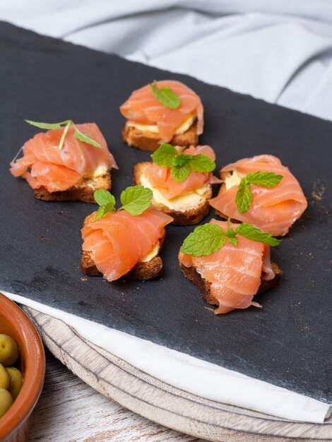 Salmone affumicato su pane tostato con burro con foglia di menta su pietra nera e vecchia tavola di legno