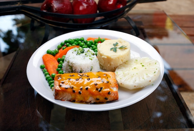 Salmone alla griglia con salsa al frutto della passione, fette di ananas, riso, purea di patate, piselli e carote