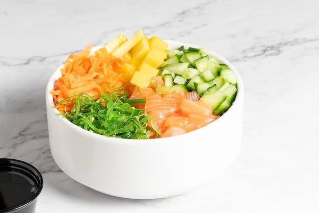 Salmone, carota, cetriolo e poke di verdure serviti in una ciotola bianca su un tavolo di marmo