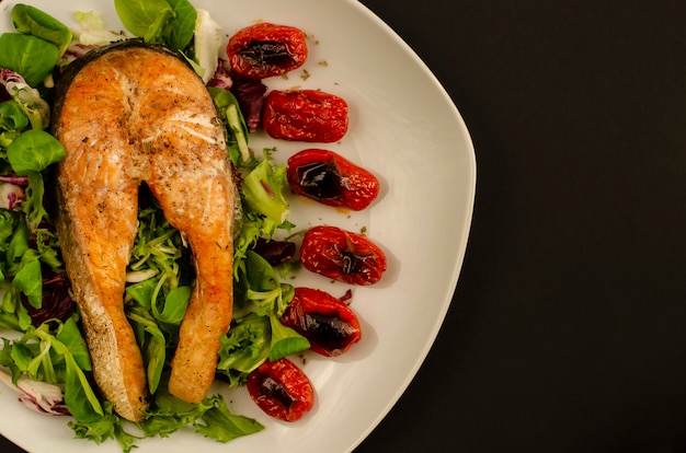 Salmone con pomodorini arrostiti e foglie di insalata mista