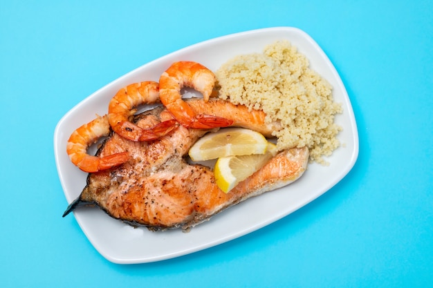 Salmone fritto con gamberi e cous-cous sul piatto bianco sul tavolo blu