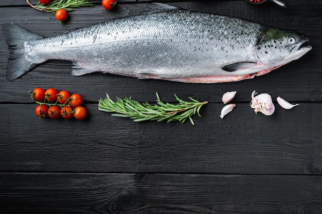 Salmone intero fresco su superficie di legno nera, vista dall'alto con spazio per il testo.