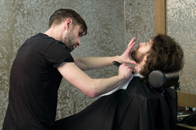 Salone da parrucchiere. Un barbiere sta radendo la barba dell'uomo con la macchina