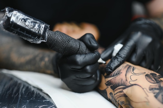 Salone del tatuaggio. Il maestro del tatuaggio sta tatuando un uomo. Macchinetta per tatuaggi, sicurezza e igiene sul lavoro. Primo piano, colorato, tatuatore.