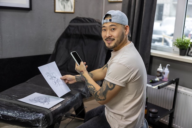 Salone di tatuaggi. Il giovane proprietario di un salone di tatuaggi asiatico si sente bene sul posto di lavoro