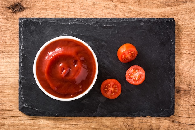 Salsa di ketchup in ciotola e pomodori sulla vista di legno del piano d'appoggio