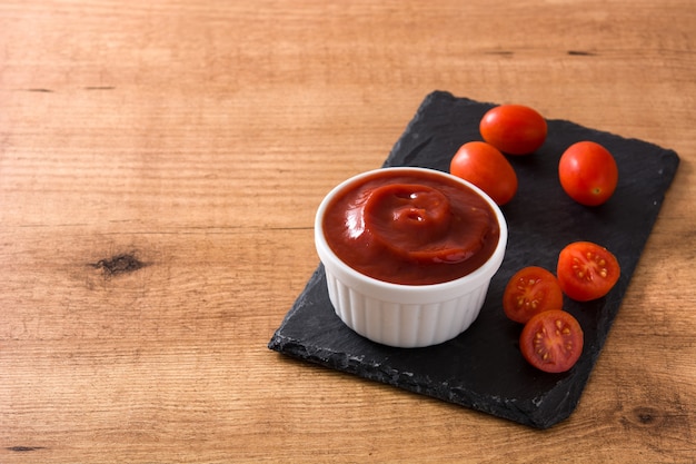 Salsa di ketchup in ciotola e pomodori sullo spazio di legno della copia della tavola