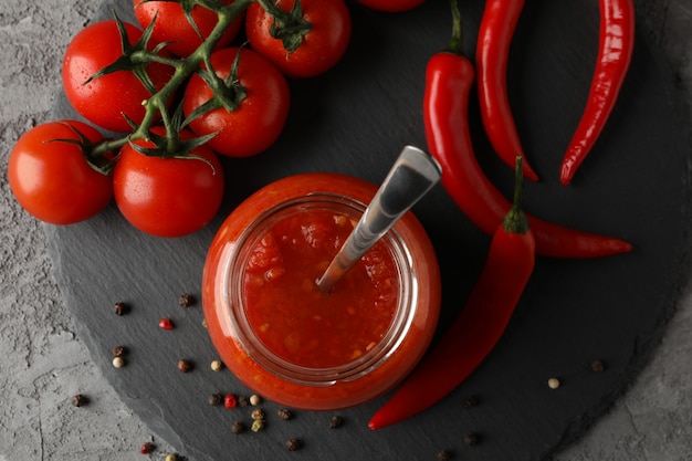 Salsa di peperoncino rosso in barattolo di vetro ed ingredienti su fondo grigio, spazio per testo. Vista dall'alto