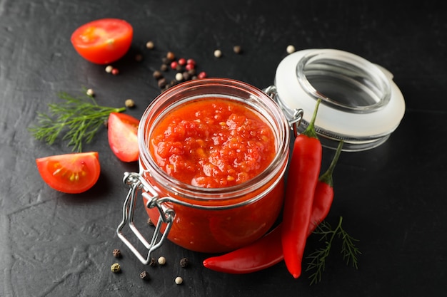 Salsa di peperoncino rosso in barattolo di vetro ed ingredienti su fondo grigio, spazio per testo. Vista dall'alto