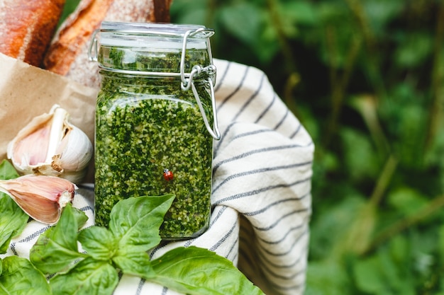 Salsa di pesto fatto in casa in un barattolo di vetro con basilico, aglio, pane all'aperto nel cestino da picnic