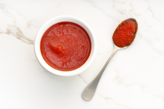 Salsa di pomodoro fresca sulla ciotola e cucchiaio sul tavolo di marmo bianco