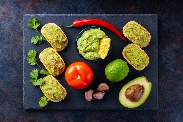 Salsa guacamole, chips di nachos e ingredienti su fondo scuro