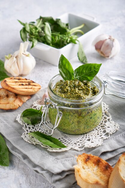 Salsa italiana tradizionale del pesto di basilico in un barattolo di vetro con i pani tostati su una tavola di pietra leggera