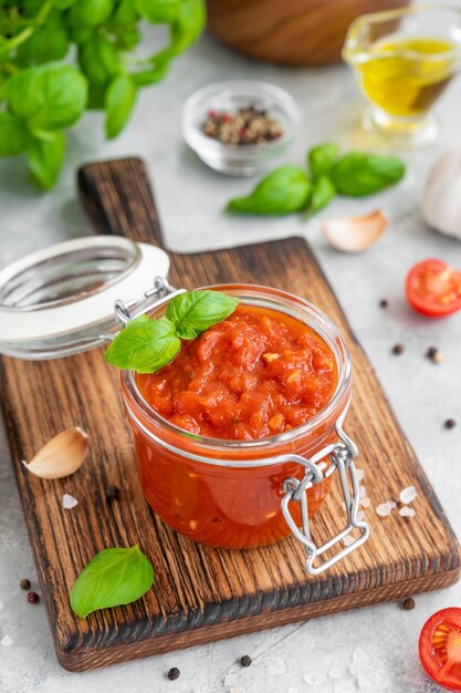 Salsa marinara italiana in un barattolo su fondo di cemento con spezie e ingredienti Spazio di copia