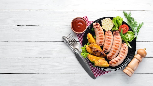 Salsicce alla griglia con patate e verdure su fondo di legno bianco Carne Vista dall'alto Spazio libero per la copia