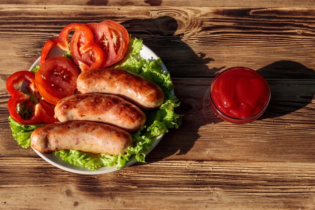 Salsicce alla griglia con verdure fresche e salsa di pomodoro su un tavolo di legno. Vista dall'alto