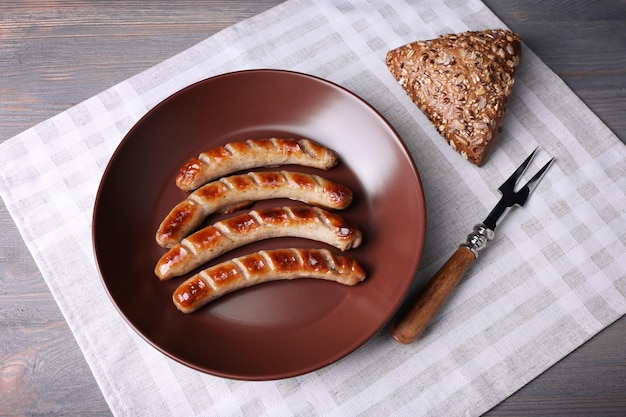 Salsicce alla griglia sul piatto con pane sul tavolo da vicino